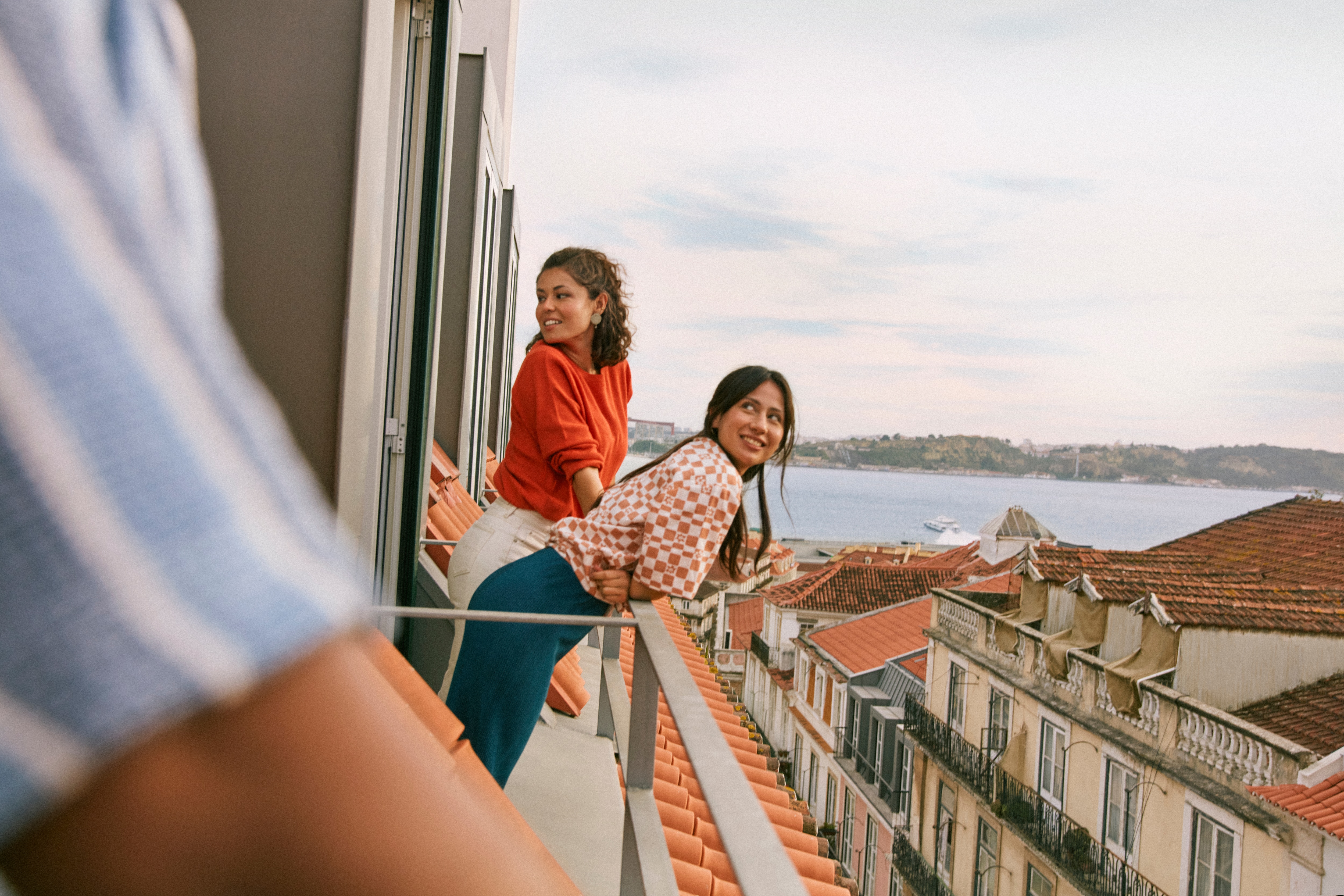 Two people stand on a balcony overlooking Lisbon with the ocean in the background.